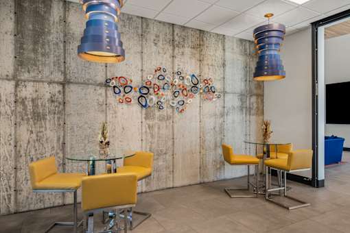 A room with a concrete wall and a glass table with yellow chairs.