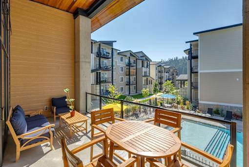 A wooden table and chairs are set up on a balcony overlooking a pool and apartment buildings.