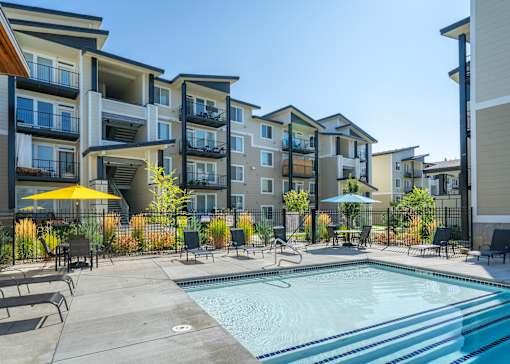 A swimming pool surrounded by lounge chairs and umbrellas in front of apartment buildings.