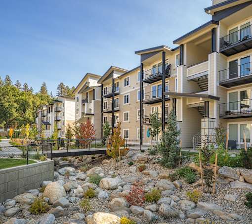 A row of modern apartment buildings with balconies and trees in the foreground.
