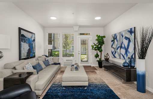 A living room with a blue rug and a large painting on the wall.