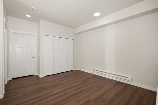 A room with white walls and wooden floors with a white door on the left and a white wardrobe on the right.