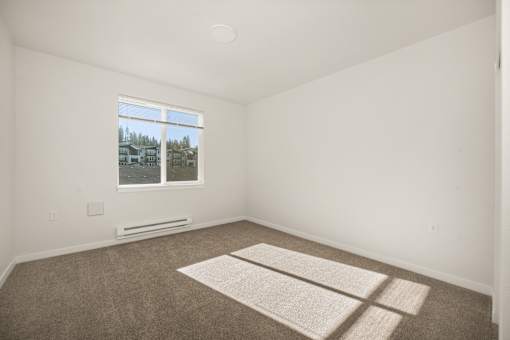 A room with a carpet and a window showing a view of houses.