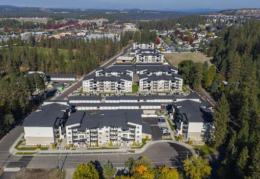 A large apartment complex is surrounded by trees and a road.