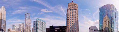 A city skyline with tall buildings and a blue sky with clouds.