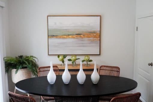 a dining room table with white vases and a painting on the wall