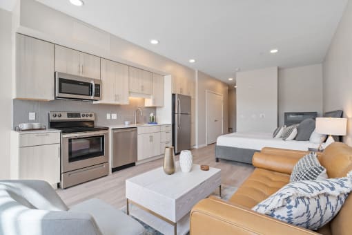 a living area with a couch coffee table and a kitchen with stainless steel appliances