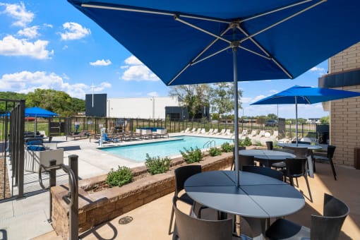 a patio with tables and umbrellas and a pool in the background