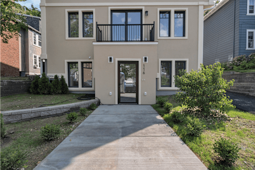 the front of a tan house with a driveway and a balcony