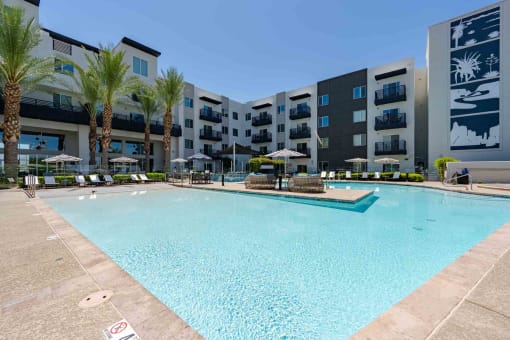 a large swimming pool with umbrellas and chairs in front of an apartment building