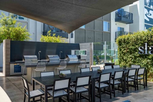 a long dining table with chairs in front of an outdoor kitchen