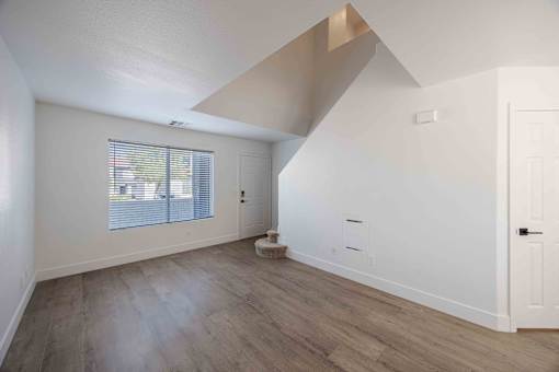 a living room with white walls and a window and wood floors