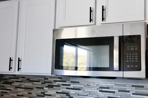 A stainless steel microwave oven is installed above a tiled backsplash in a kitchen.