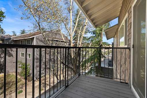 A balcony with a black railing and a view of a house and trees.