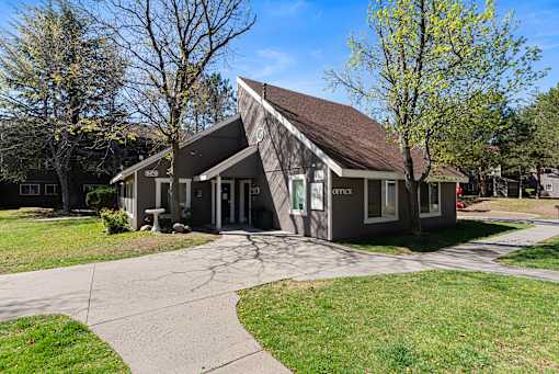 A building with a brown roof and a sign that says "OFFICE" is surrounded by trees and grass.
