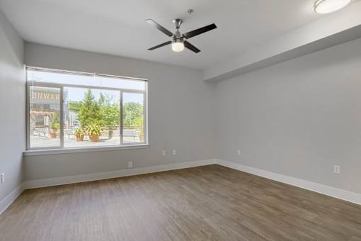 A room with a ceiling fan and a window showing a view of a storefront.