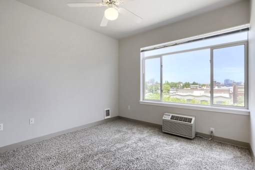 A room with a ceiling fan, carpeted floor, and a window overlooking a cityscape.
