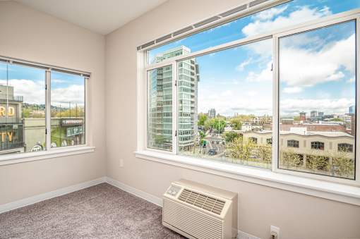 A room with a window showing a view of a cityscape and a wall-mounted air conditioner.