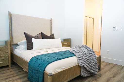 A bed with a white sheet and a blue blanket is in the foreground of a room with a wooden headboard at Zora Encanto, Arizona