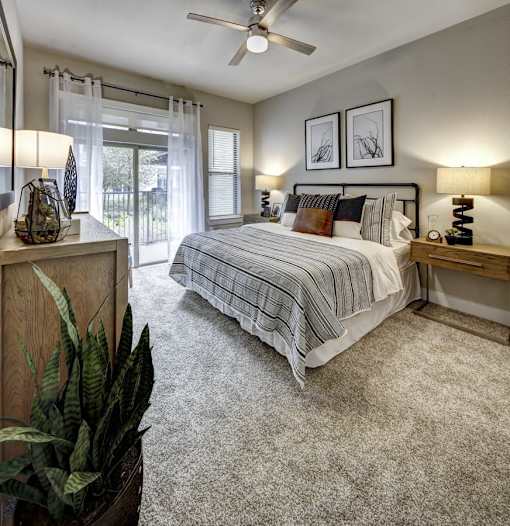 A bedroom with a bed, nightstands, and a ceiling fan at Arise Riverside Apartments, Austin, Texas
