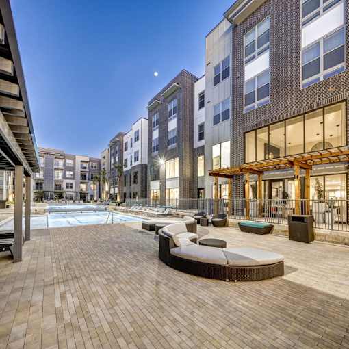 A modern outdoor pool area with a wooden deck and lounge chairs at Arise Riverside Apartments, Texas