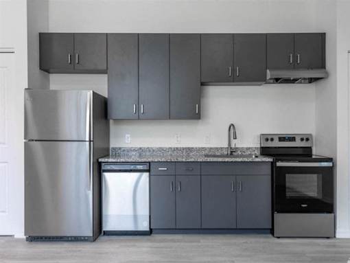 A modern kitchen with a stainless steel refrigerator, a dishwasher, a sink, and a stove.