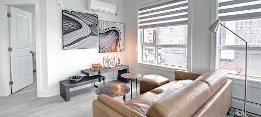 A living room with a brown leather couch, a black and white abstract painting on the wall, and a window with blinds.