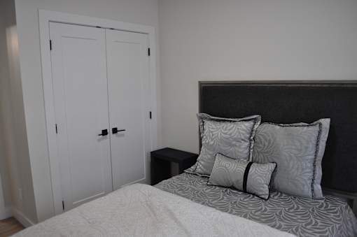 A bed with a white comforter and two pillows sits in a room with a white closet at The Laurent at Laurel Apartments, Edmonton, Alberta