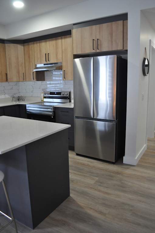 A modern kitchen with a stainless steel refrigerator and wooden cabinets at The Laurent at Laurel Apartments, Alberta