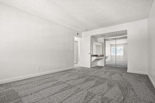 A room with a carpeted floor and a glass door leading to a balcony.