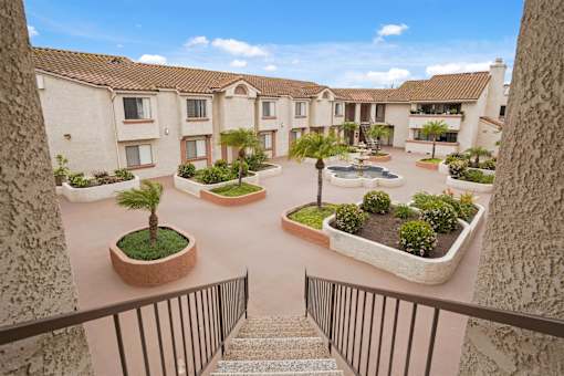 A view of a courtyard with a fountain and plants from a balcony.