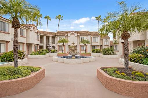 A courtyard with palm trees and a fountain in the middle of apartment buildings.