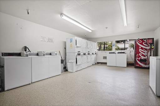 A Coca Cola vending machine sits in a white room with a washing machine and dryer.