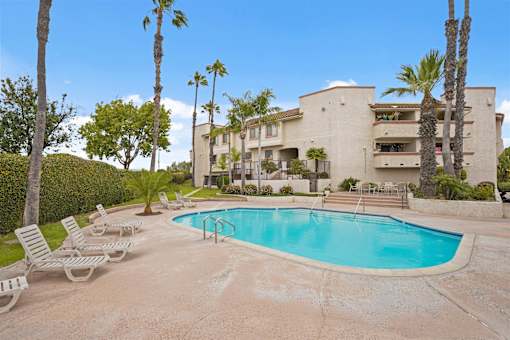 A swimming pool surrounded by palm trees and lounge chairs in front of a building.