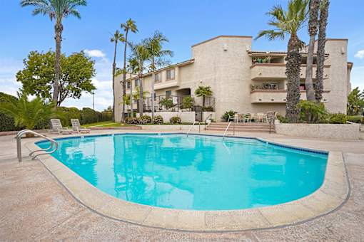 A swimming pool in front of a building with palm trees.