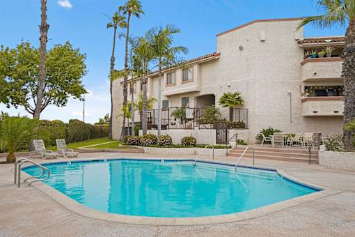 A swimming pool in front of a building with palm trees.
