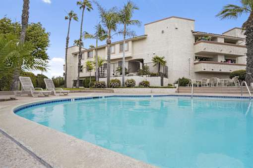 A swimming pool in front of a building with palm trees.
