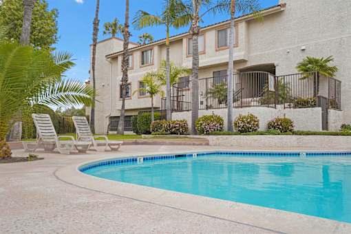 A swimming pool in front of a building with palm trees.