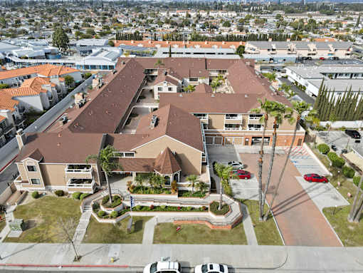 A large building with a brown roof is surrounded by a parking lot and palm trees.