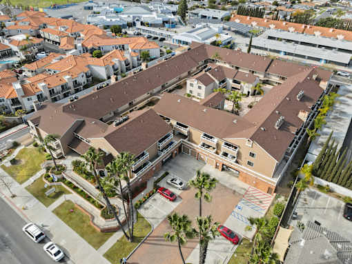 A large building with a brown roof is surrounded by smaller buildings and palm trees.