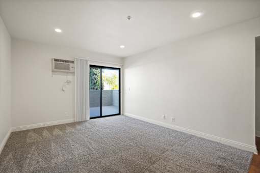 A spacious room with a carpeted floor and a sliding glass door leading outside.