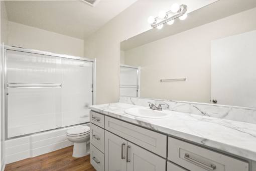 A white bathroom with a marble counter top and a walk in shower.