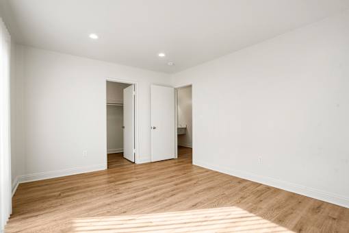 A room with white walls and wooden flooring with a doorway open to another room.