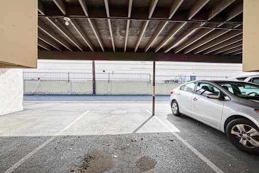 A white car is parked in a parking lot under a covered area.