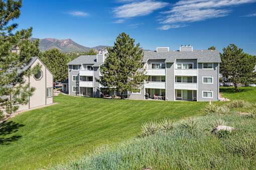 A large grey building with a green lawn in front.