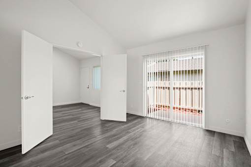A room with white walls and a grey floor with a white door open.