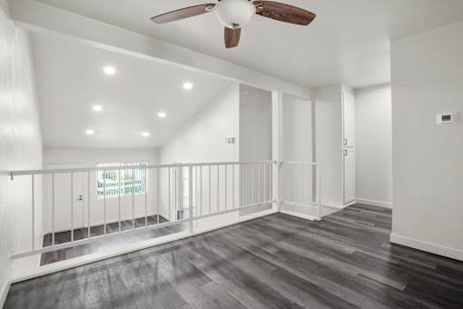 A spacious room with a ceiling fan and wooden flooring.