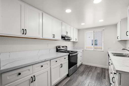 A kitchen with white cabinets and a marble countertop.