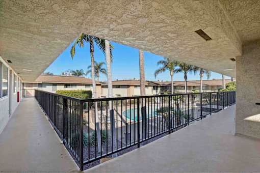 A balcony with a black railing and a pool in the background.
