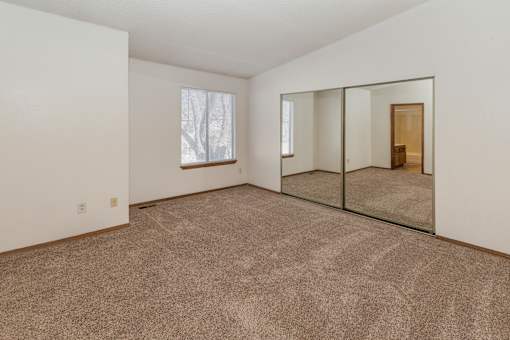 A large empty room with a carpeted floor and a large mirror on the wall.